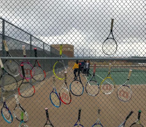 Tennis players hang their rackets on the fence during practice.
