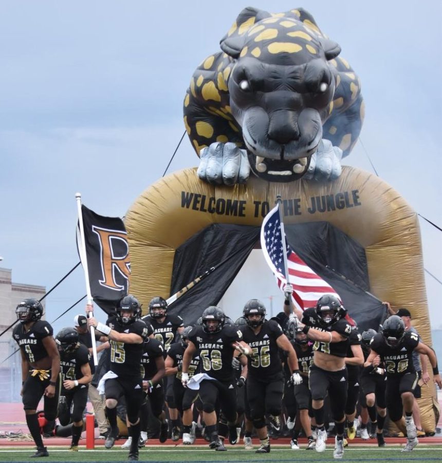 Varsity quarterback Luke Wennogle ‘23 and middle linebacker Ryland Mill ‘23 hold up the Rock Canyon flag and the American flag as they run through the Jaguar tunnel during their opening game Aug. 25. Inside the tunnel, everyone is pumped up banging on the side waiting to hear [the song] Welcome to the Jungle and for the curtains to open because everyone knows its game time, Mill said. 