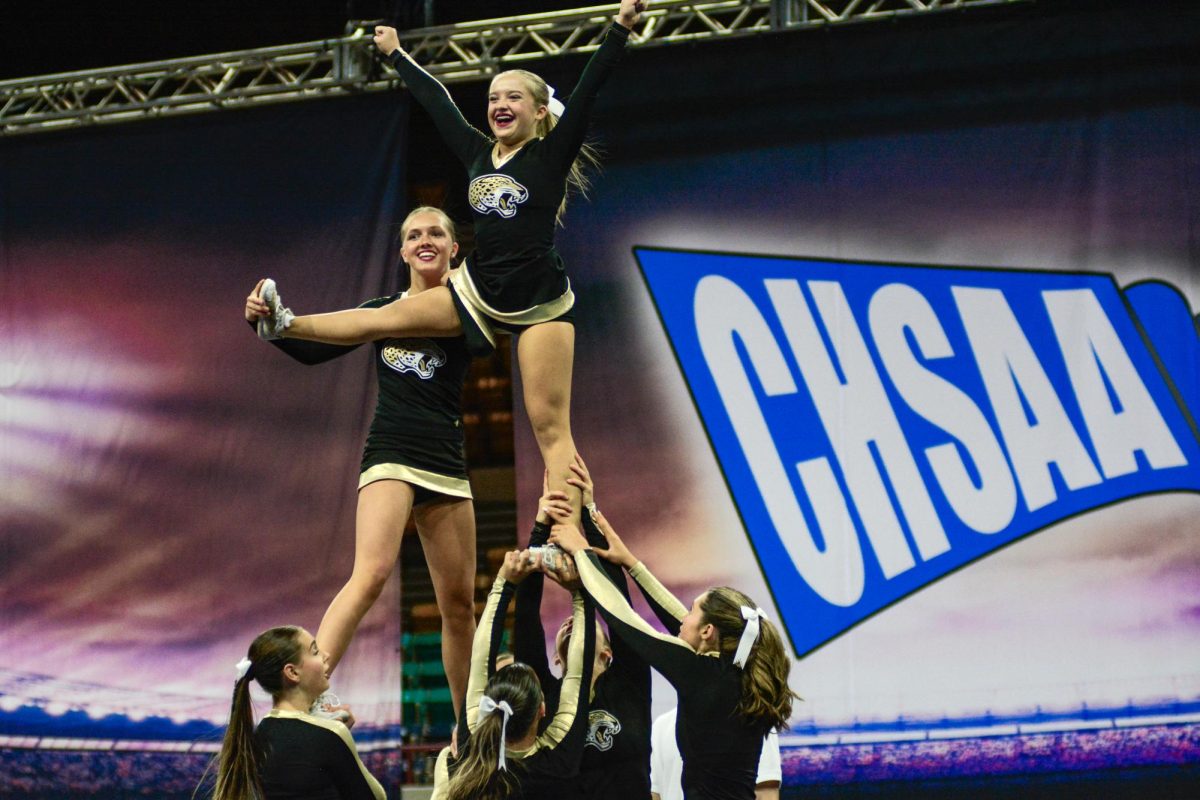Stunting in front of the CHSAA poster, varsity bracer Allison Arro ‘25 holds up flyer Riley Gehrke ‘27 during the single base hand in hand Dec. 9. The single base hand in hand is considered the most difficult part of the team’s routine because it’s where they are able to score the most points in difficulty. “In cheerleading, we use a term called ‘hitting zero’,” varsity base Emerson Lindsley ‘25 said. “[It] basically means you go out and hit your routine with zero deductions, no falls, all stunts in the air, all tumbling landed. Usually, the teams that hit zero have the highest placement, since they had the least amount of deductions. Difficulty and execution are also very important point boosters in cheerleading.”
