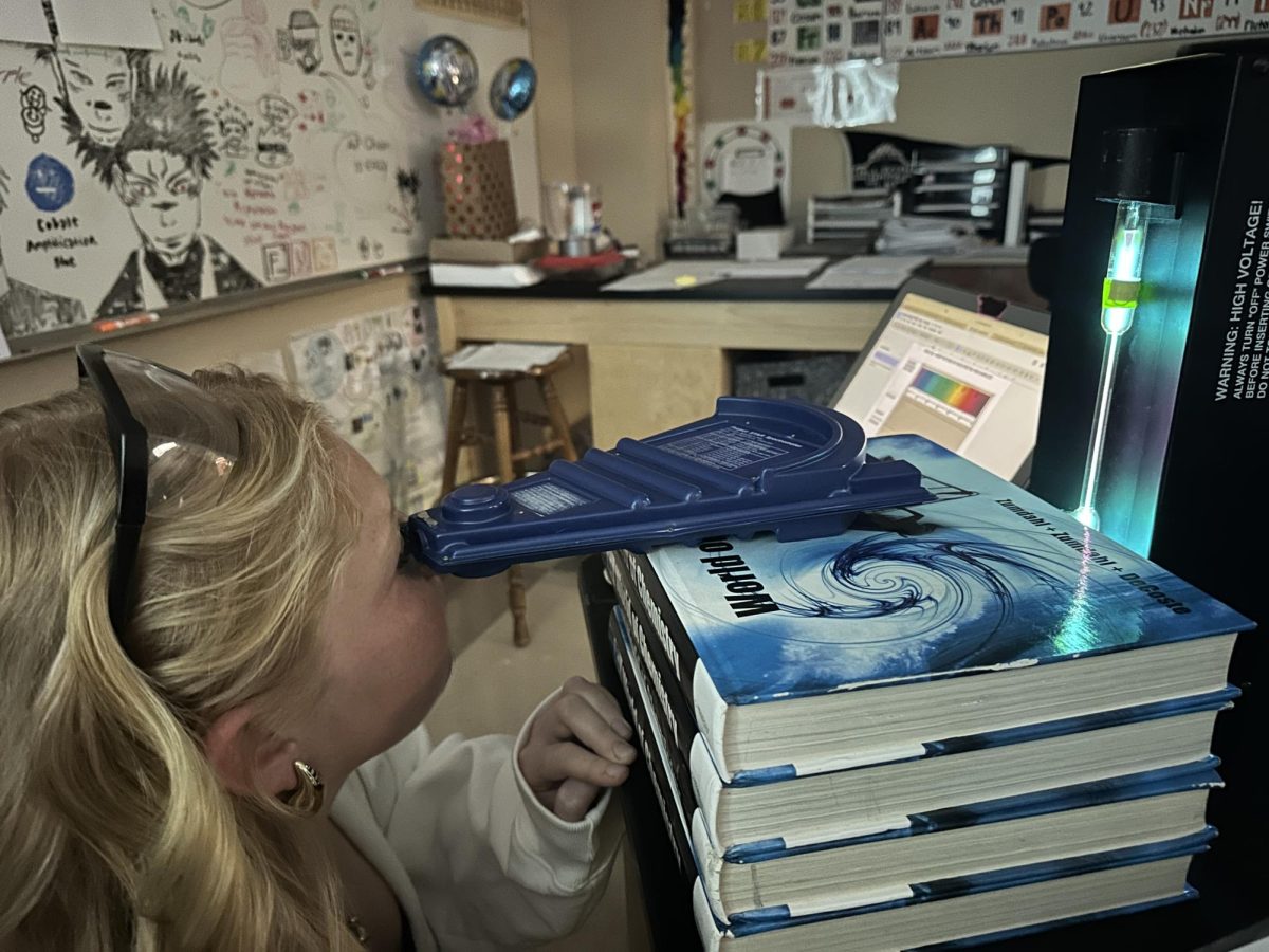 During a lab in Kerry Reilly’s Chem Honors class, Millie Goblirsch ‘27 looks through a spectroscope to examine the emission spectra of a mystery element Nov. 12. Through spectral tubes and flame tests, students were able to discover the wavelengths of different elements and metals via the unique emission spectra that each element produces. “I liked the chem lab because we were able to see how certain elements reacted when energy was added,” Addison Evert ‘27 said. “Many of the flames were unique colors when the metals were added.”
