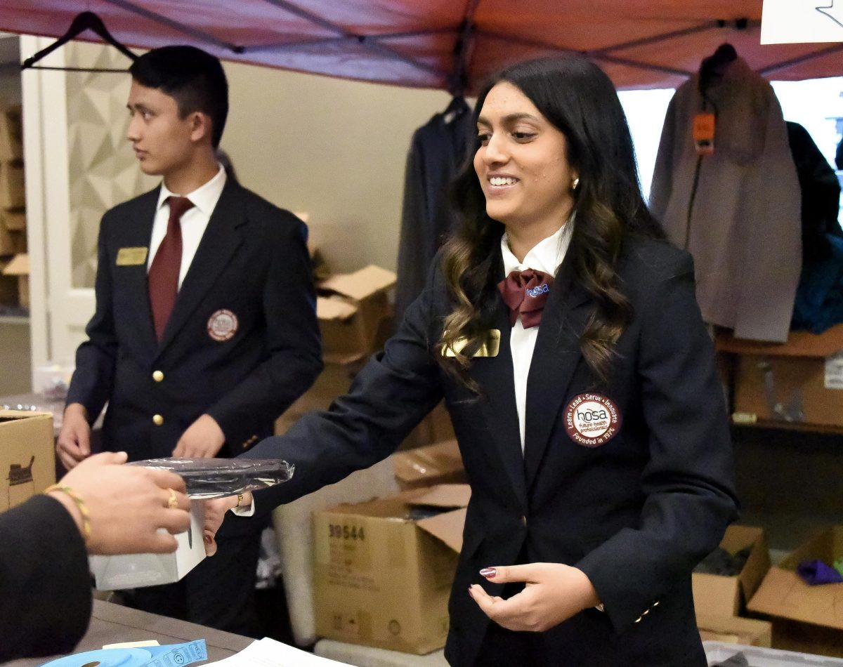 State President Medha Kuntamukkla ‘25 gives out a backpack at the HOSA Store Feb. 18. Backpacks and water bottles were free for SLC attendees and exchanged for red tickets given to students at the beginning of the conference. Other HOSA merchandise was available for purchase and could be bought throughout the conference. “I had to make sure everything was running smoothly and be there as support for the members,” Kuntamukkla said. “If they had any questions, I would direct where to go, and also just helped out with registration, making sure all the chapters were checking in okay and they were all getting their rooms.” 